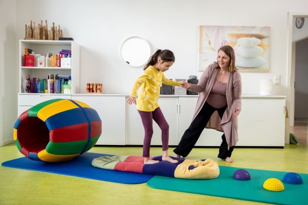 Therapieraum der Praxis: Kind balanciert über einen Bewegungsparcours, begleitet von Tania Gallardo